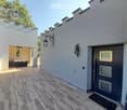 A modern outdoor area with tiled flooring, a grey front door, decorative wall-mounted lanterns, and a small seating area with a black bench and a small table.