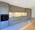 Modern kitchen with grey cabinets, stainless steel sink, built-in oven, and integrated lighting.