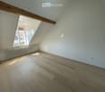 Unfurnished Room. Empty attic room with wooden flooring, white walls, exposed wooden beams, and a window letting in natural light.