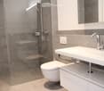 Modern bathroom with a white sink, chrome faucet, toilet, and a glass-enclosed shower area with a built-in seat.
