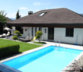 Modern house with brown roof, white walls, swimming pool, garden, lounge chairs, umbrellas
