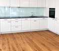 Modern kitchen with white cabinets, wooden flooring, and a black countertop. Features a sink, faucet, and built-in oven.