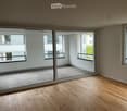 Empty room with wooden flooring, large sliding glass doors leading to a balcony area, and large windows providing natural light.