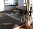 Modern balcony with wooden floor, glass railing, small table and chair, and a view of the building exterior.