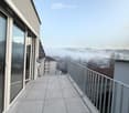 Balcony with concrete tiles, metal railing, and a view of a misty landscape and buildings.