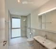 Modern bathroom with a white sink, mirror, toilet, and glass-enclosed shower area. Features recessed lighting and sleek fixtures.