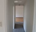 Empty hallway with tiled floor and white walls, leading to another room with wooden flooring visible at the end.