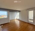 Empty room with wooden flooring, large windows, and a sliding glass door leading to a balcony.