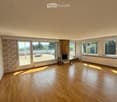 Empty room with wooden flooring, large windows, and a fireplace. The room has a balcony accessible through large glass doors.