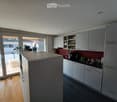 Modern kitchen with white cabinets, dark countertops, and a central island. Features include a coffee maker, cups, and a small plant on the counter.