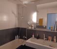 Modern bathroom with a bathtub, showerhead, sink, and various toiletries including toothpaste, soap, and a mirror. The walls are tiled in white and dark gray, and there is a towel hanging on the side.