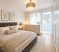 Modern bedroom with a large bed, nightstand, drawer unit, table lamp, floor lamp, picture frames, and a small plant on the windowsill.