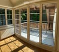 Bright, spacious balcony with large glass doors, wooden flooring, and a view of greenery outside.