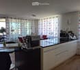 Modern kitchen with white cabinets, black countertops, coffee machine, microwave, blender, and a small dining area with a table and chairs.