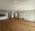 Empty room with light-colored walls, wooden flooring, and white cabinetry in the background. No furniture or personal items are present.
