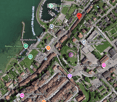 Aerial view of a town with buildings, streets, and a waterfront area with a marina. Visible landmarks include a hotel, school, and recreational areas.