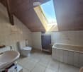 Bathroom with a toilet, bathtub, sink, and mirror. The room features tiled walls and a skylight window, with a wooden ceiling and a towel hanging on the side.