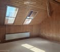 Empty room with wooden walls and ceiling, skylight windows, and a radiator on one wall.