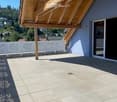Balcony with wooden roof, tiled floor, white railing, and large window opening to the interior.