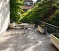 Balcony with tiled floor, metal railing, small round table, four chairs, and several flower boxes.