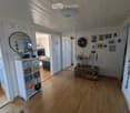 Cozy hallway with wooden flooring, white walls, and various decorative items including a mirror, framed photos, and a small table with candles and a wreath.