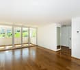 Empty room with wooden flooring, white walls, large sliding glass doors, and a view of a green landscape.