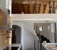 Modern kitchen with black marble flooring, white countertops, stainless steel appliances, and a sleek staircase leading to an upper level with wooden beams and skylights.