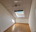 Empty room with wooden herringbone flooring, white walls, and a skylight window letting in natural light. The ceiling features wooden paneling and integrated lighting fixtures.