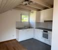Modern kitchen with white cabinets, stainless steel sink, dishwasher, and oven. Wooden flooring and tiled backsplash.