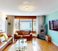 Modern living room with two leather sofas, a glass coffee table, a fireplace, a TV, and decorative plants.