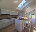 Modern kitchen with white cabinets, wooden accents, island, and stools, featuring a skylight and a view of the garden.