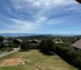 Panoramic view of a rural landscape with houses, trees, and distant mountains under a clear blue sky.