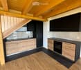 Modern kitchen with wooden beams, black countertops, and stainless steel appliances. Features include a sink, oven, and wooden cabinets.
