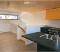 Modern kitchen with black countertops, stainless steel sink, stove, and orange cabinets.