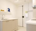 Modern, minimalist kitchen with white cabinets, a stainless steel sink, and a built-in oven. The space features sleek countertops, a small art piece on the wall, and a few decorative items on the shelves.
