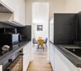 Modern kitchen with black countertops, stainless steel appliances, and a dining area with colorful chairs.