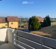 Balcony with white railing overlooking a rural landscape with houses, trees, and open fields.