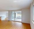 Bright, empty room with wooden flooring, white walls, large windows, and a sliding glass door leading to a balcony.