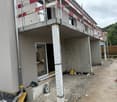 Under-construction building with exposed concrete structure, scaffolding, and construction materials on the ground.