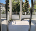 Spacious balcony with white railings, concrete floor, and views of greenery and neighboring buildings.