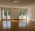 Empty room with wooden flooring, large sliding glass doors leading to a balcony, white walls, and natural light.