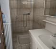 Bathroom with beige tiled walls and floor, a white sink with a faucet, a bathtub, a mirror, a radiator, and a bottle on the floor.