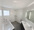 White tiled walls, bathtub, double sink, toilet, mirror, shower head
