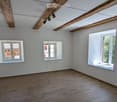 Empty room with wooden flooring, white walls, and three windows, including a large window with a view of greenery.