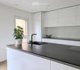 Modern kitchen with white cabinets, dark grey countertop, sink, faucet, and a potted plant on the island.
