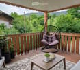 Balcony with wooden decking, hanging wicker chair, coffee table, potted plants, and scenic view of greenery.