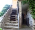 A narrow stone staircase leads up to a doorway, flanked by stone walls and greenery, with a metal railing on one side.