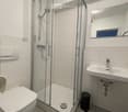 Modern bathroom with white tiles, a glass-enclosed shower, a toilet, a sink, and a mirror.