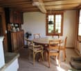 Cozy dining area with wooden table, chairs, and built-in wooden cabinetry. Features a hanging pendant light, a small fan, and a pet bed in the corner.