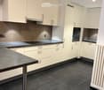 Modern kitchen with white cabinets, dark countertops, and black tiled flooring. Features a sink, oven, and stove.